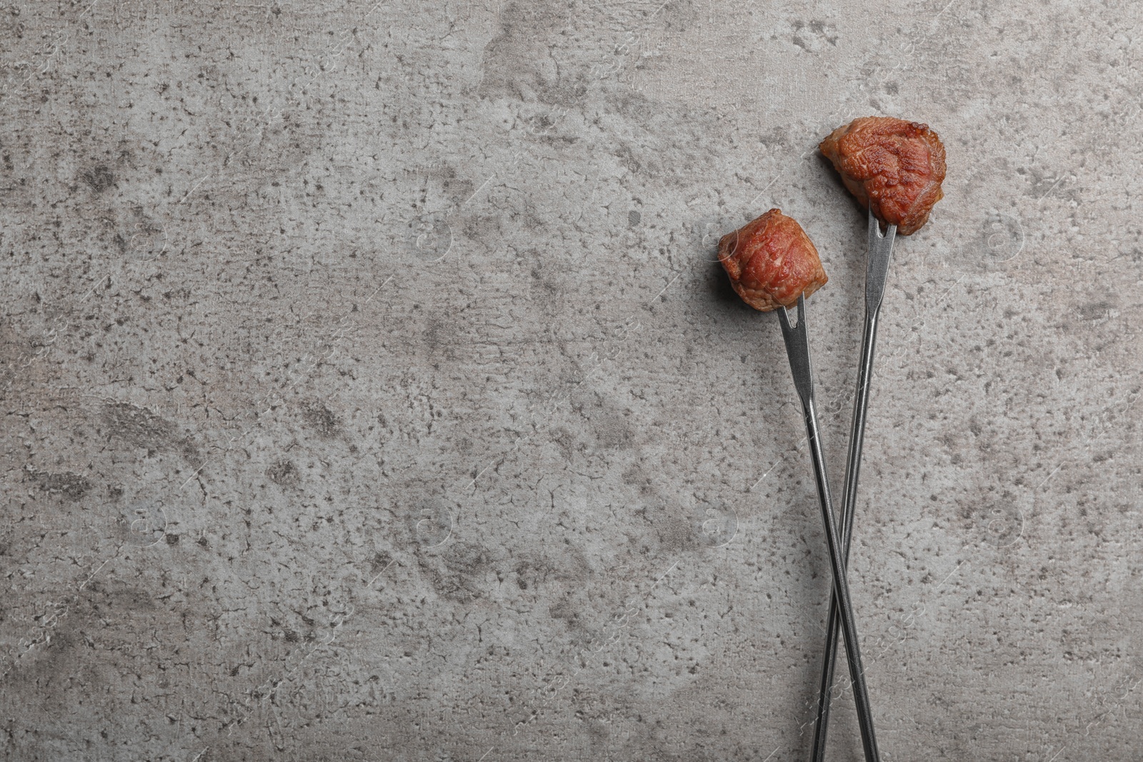 Photo of Forks with fried meat fondue pieces on grey background, top view. Space for text