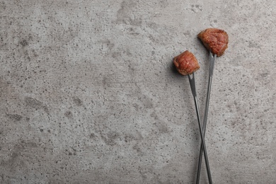 Forks with fried meat fondue pieces on grey background, top view. Space for text