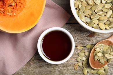 Photo of Bowl of oil and pumpkin seeds on wooden table, flat lay