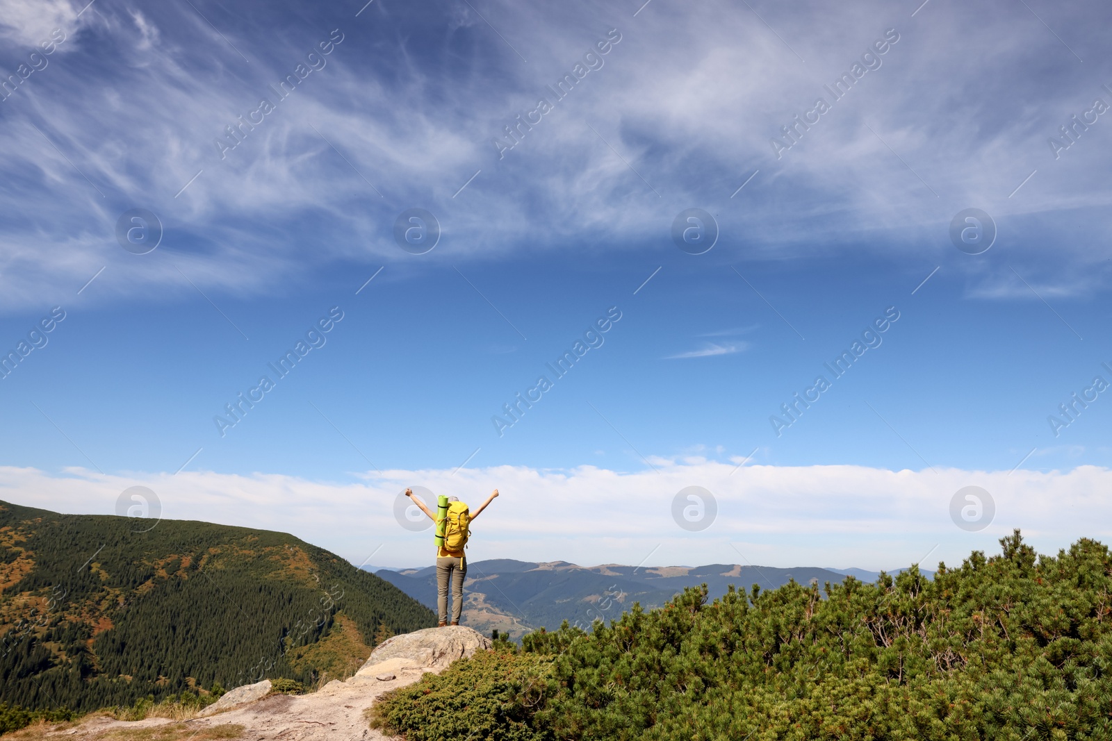 Photo of Young woman with backpack on rocky peak in mountains, back view