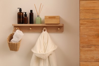 Photo of Wooden shelf with toiletries, fresh towel and bathrobe on beige wall. Interior element