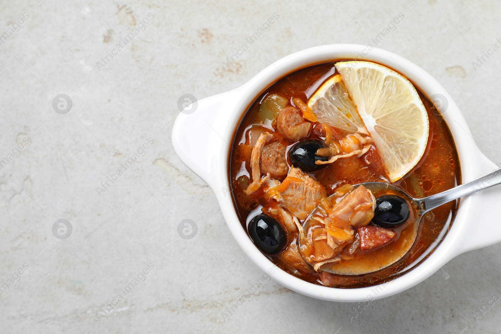 Photo of Meat solyanka soup with sausages, olives, vegetables and spoon in bowl on white textured table, top view. Space for text