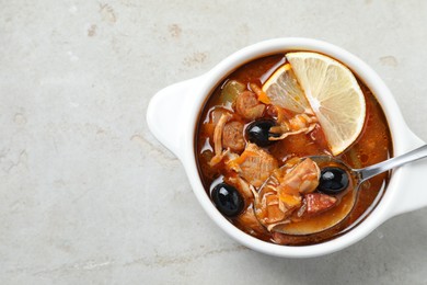 Meat solyanka soup with sausages, olives, vegetables and spoon in bowl on white textured table, top view. Space for text