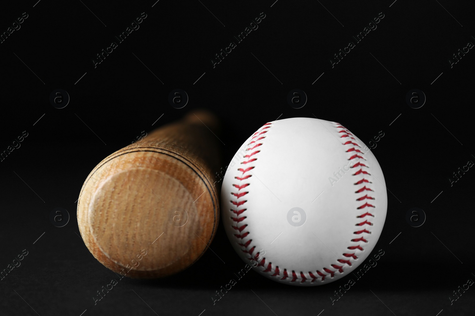 Photo of Wooden baseball bat and ball on black background, closeup. Sports equipment