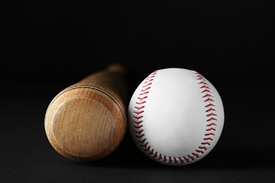 Photo of Wooden baseball bat and ball on black background, closeup. Sports equipment