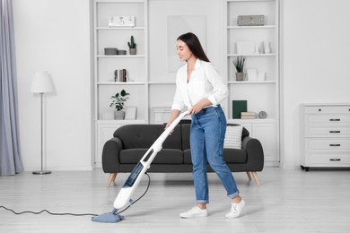 Photo of Happy woman cleaning floor with steam mop at home