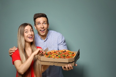 Attractive young couple with delicious pizza on color background