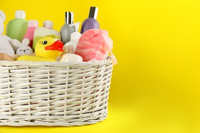 Photo of Wicker basket with baby cosmetic products and accessories on yellow background. Space for text