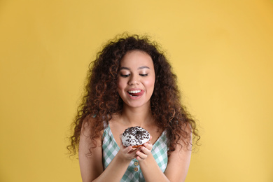 Photo of Beautiful African-American woman with donut on yellow background