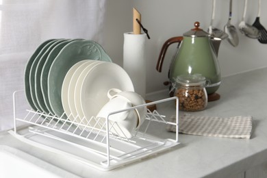 Photo of Drainer with different clean dishware and cups on white table in kitchen