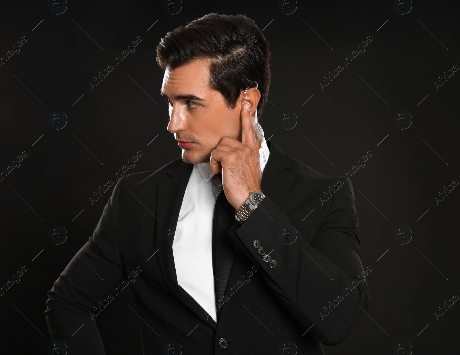 Photo of Male security guard in uniform using radio earpiece on dark background