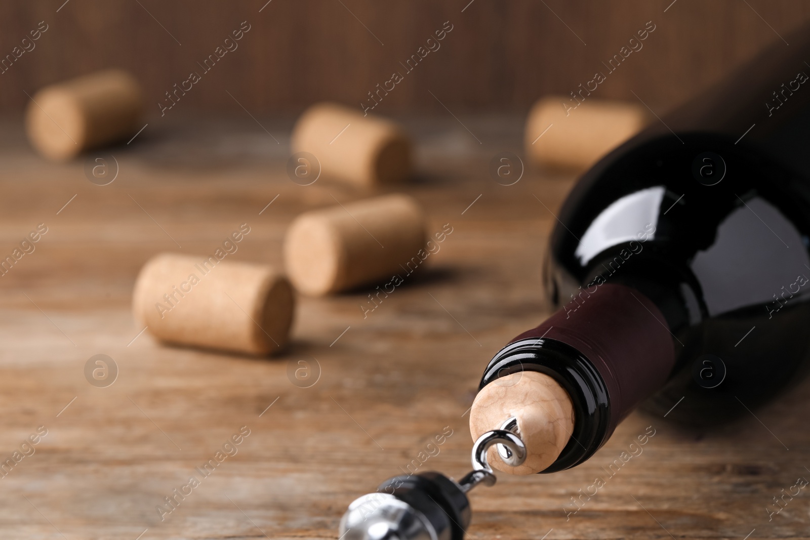 Photo of Opening wine bottle with corkscrew on wooden table, closeup. Space for text