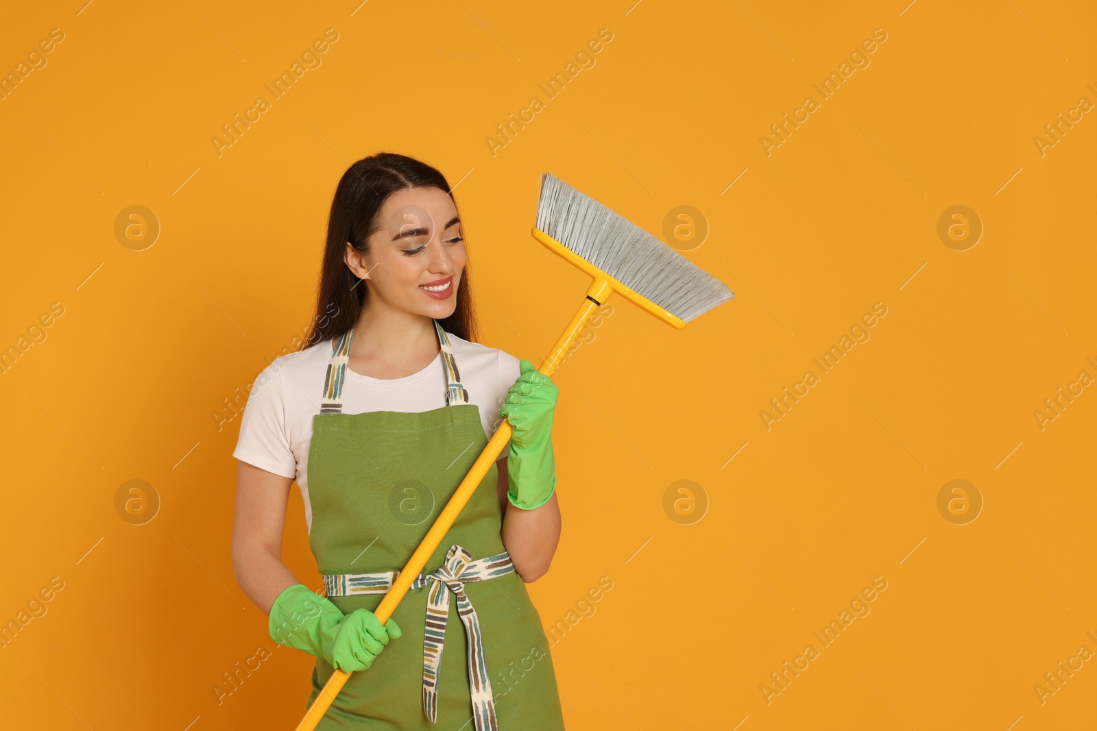 Photo of Beautiful young woman with broom on yellow background. Space for text