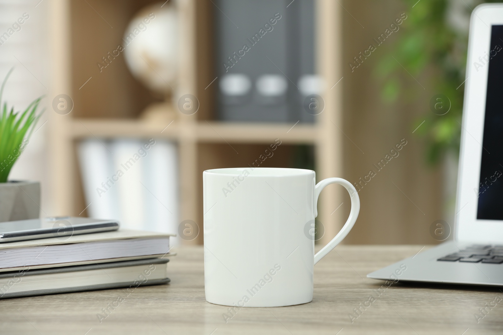 Photo of White ceramic mug and notebooks on wooden table indoors