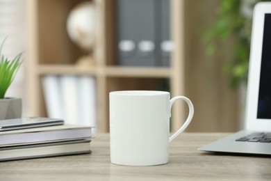 Photo of White ceramic mug and notebooks on wooden table indoors