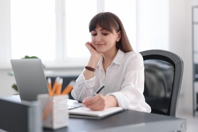 Woman taking notes during webinar at table indoors