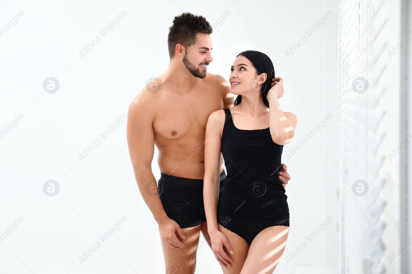 Photo of Young couple in black underwear near window indoors