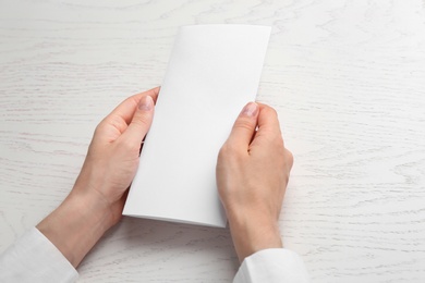 Photo of Young woman holding blank brochure at white wooden table, closeup. Mock up for design