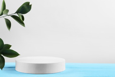 Photo of Green leaves and round shaped podium on light blue wooden table against white background. Space for text