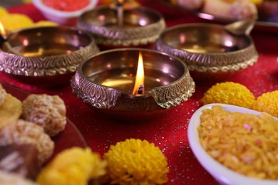 Photo of Diwali celebration. Beautiful composition with diya lamps, tasty Indian sweets and bright rangoli on shiny red table, closeup