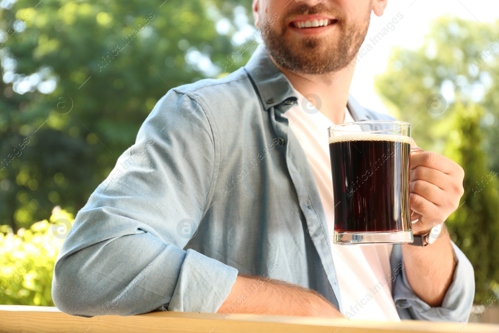 Photo of Young man with cold kvass outdoors, closeup. Traditional Russian summer drink