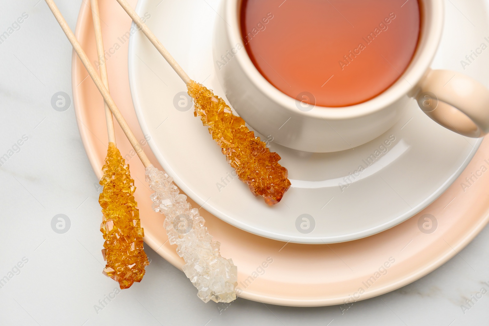 Photo of Sticks with sugar crystals served to tea on white marble table, top view