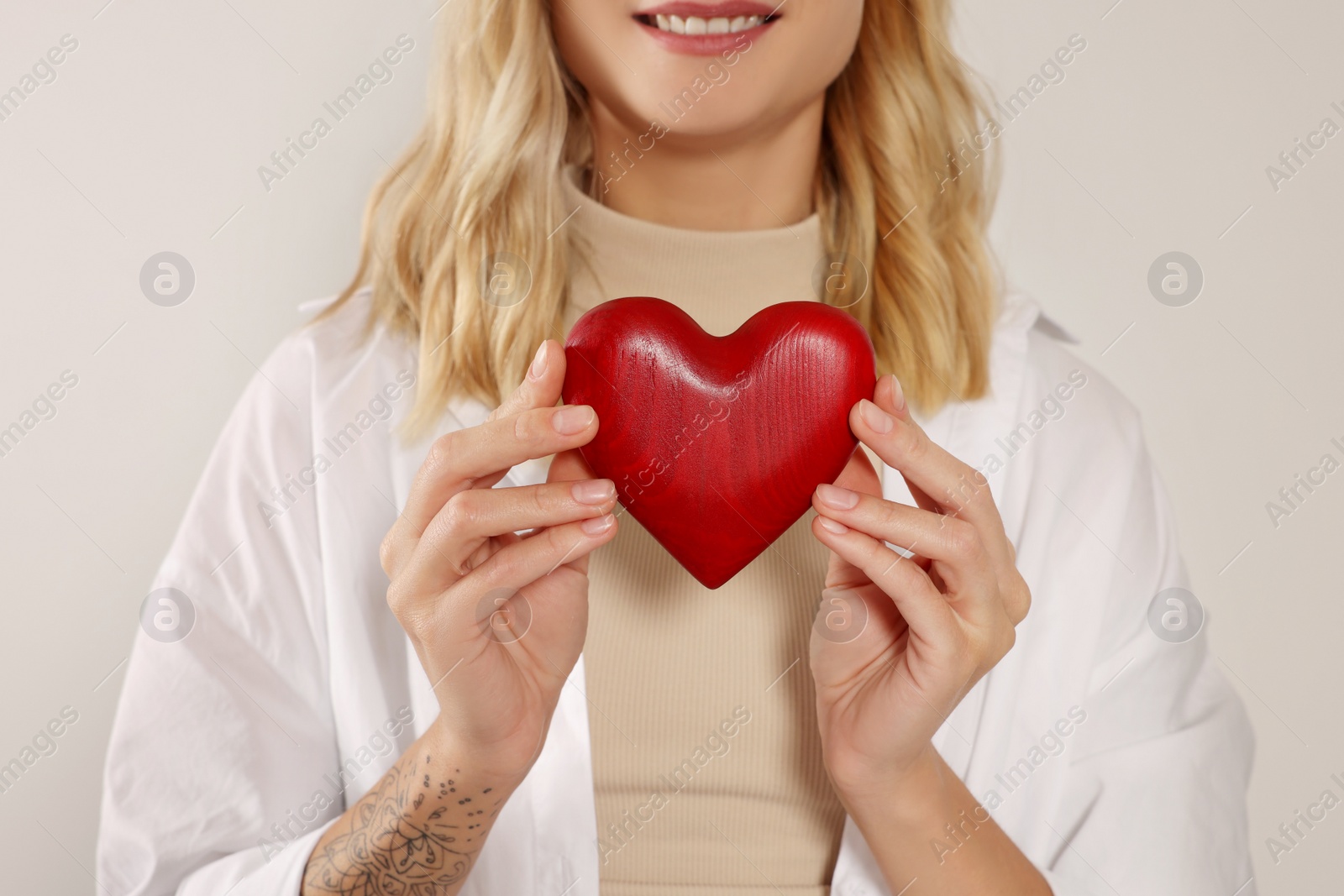 Photo of Happy volunteer holding red heart with hands on light background, closeup