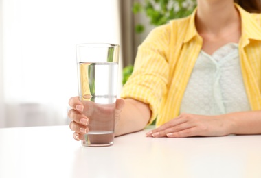 Woman holding glass of water at white table, closeup. Refreshing drink