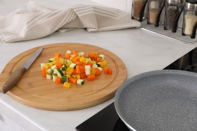 Photo of Wooden board with cut vegetables and knife near frying pan in kitchen