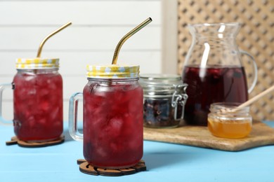 Delicious iced hibiscus tea on light blue wooden table, space for text