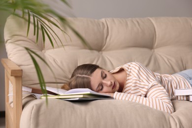 Young tired woman sleeping near books on couch indoors