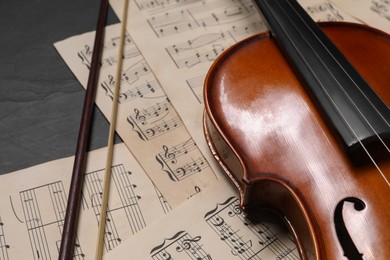 Photo of Violin, bow and music sheets on black table, closeup