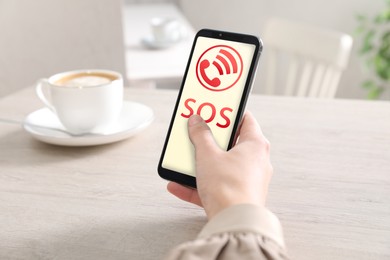 Image of Woman holding smartphone with emergency call SOS on screen indoors, closeup