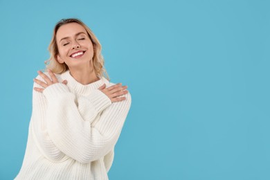 Happy woman in stylish warm sweater on light blue background. Space for text