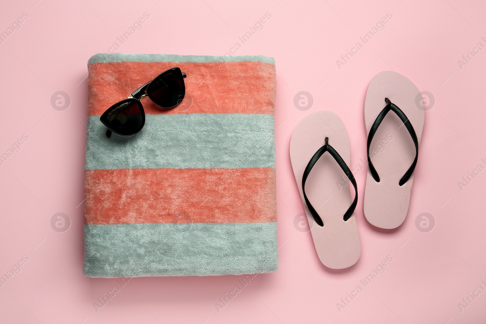 Photo of Beach towel, flip flops and sunglasses on pink background, flat lay