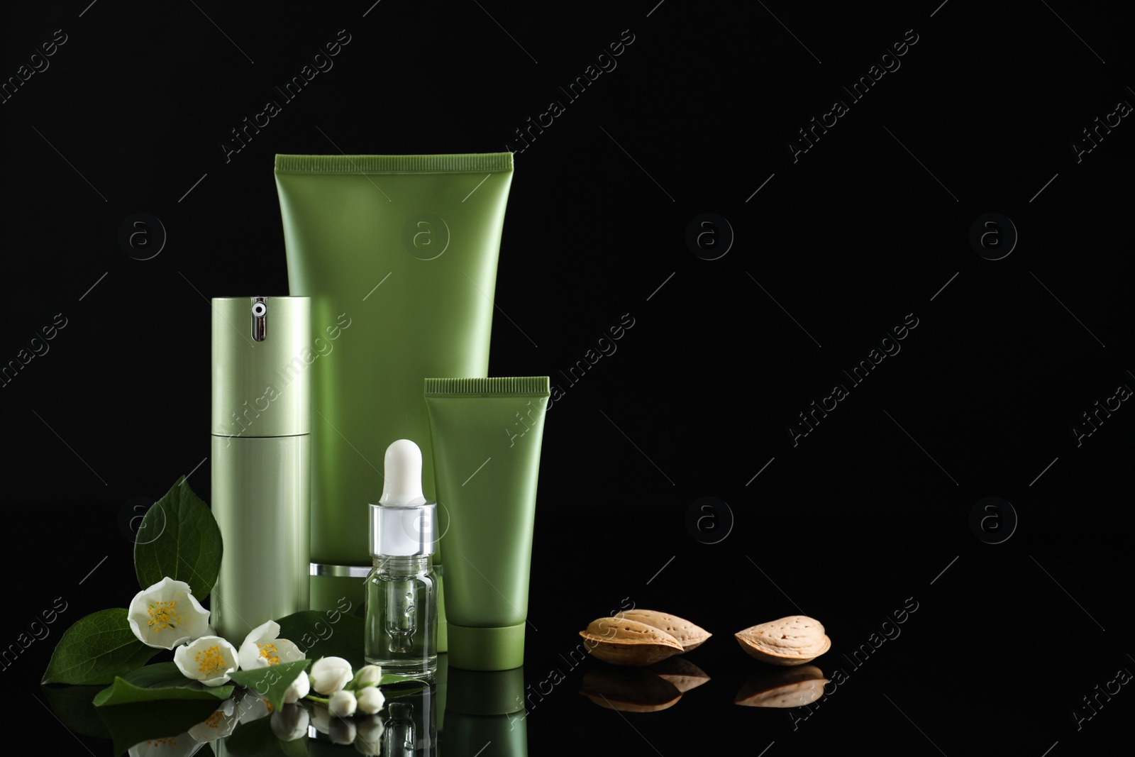 Photo of Set of cosmetic products, almond nuts and flowers on black background, space for text