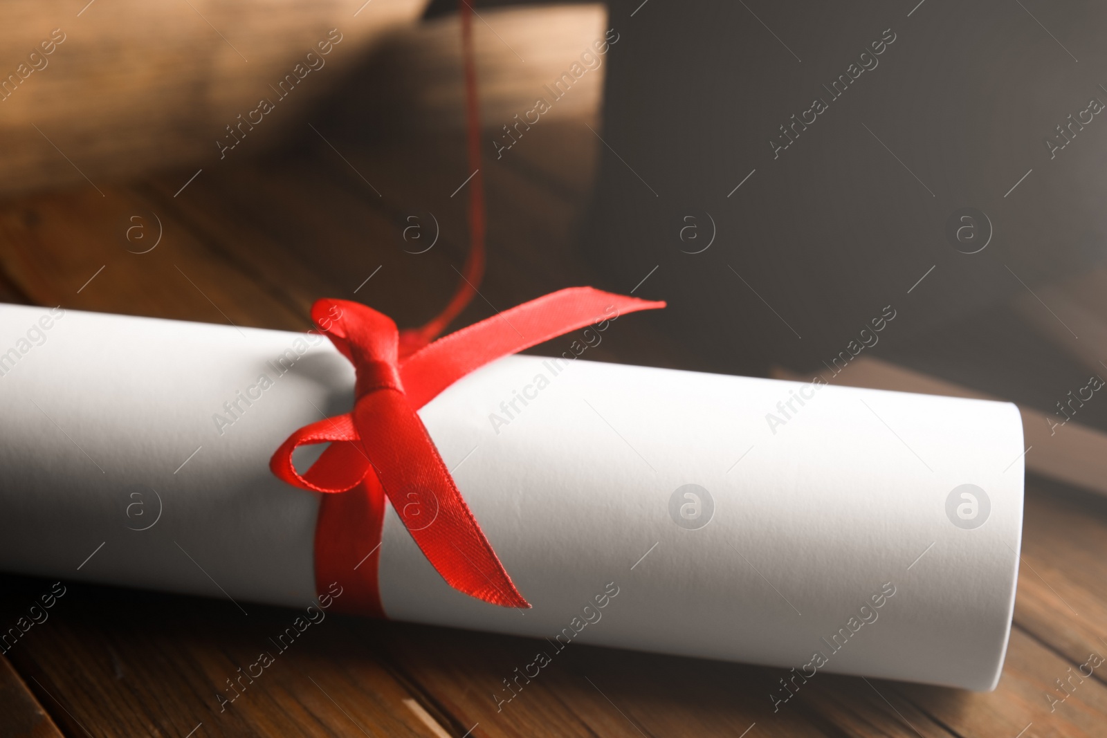 Photo of Graduation hat and student's diploma on wooden table, closeup