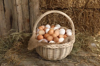 Photo of Wicker basket with fresh chicken eggs and dried straw in henhouse
