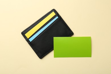 Photo of Leather business card holder with colorful cards on beige background, top view