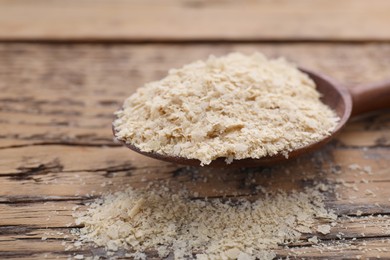 Photo of Spoon of brewer`s yeast flakes on wooden table, closeup