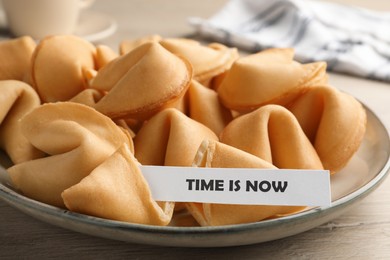 Tasty fortune cookies with prediction Time in now in plate on wooden table, closeup