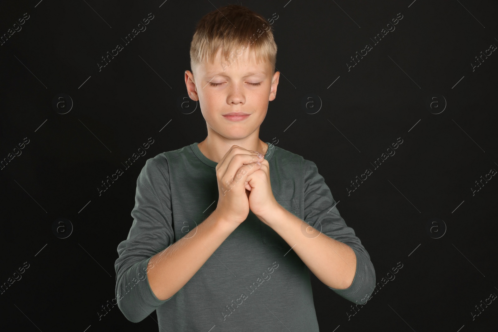 Photo of Boy with clasped hands praying on black background