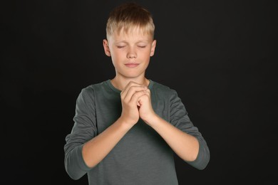 Photo of Boy with clasped hands praying on black background