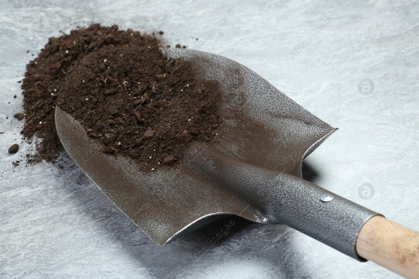 Metal shovel with fertile soil on gray textured surface, closeup Photo of Metal shovel with fertile soil on gray textured surface, closeup