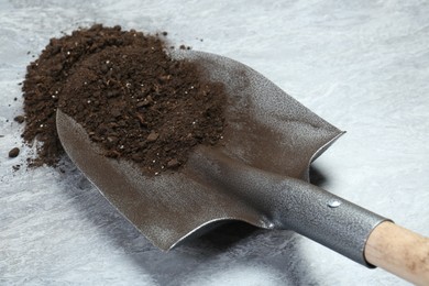 Photo of Metal shovel with fertile soil on gray textured surface, closeup