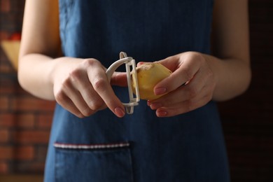 Woman peeling fresh potato indoors, closeup view