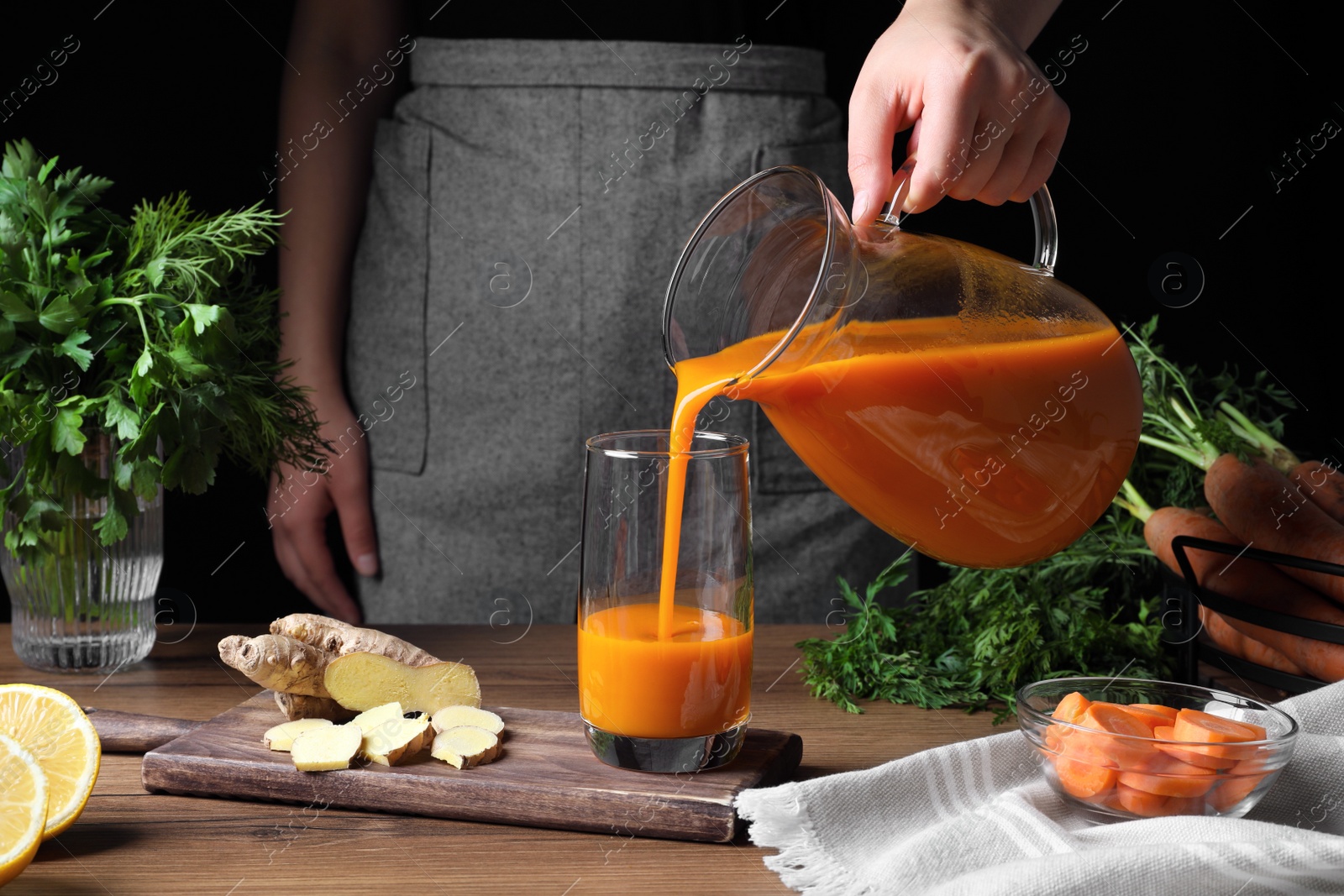 Photo of Woman pouring carrot juice from jug into glass at wooden table, closeup