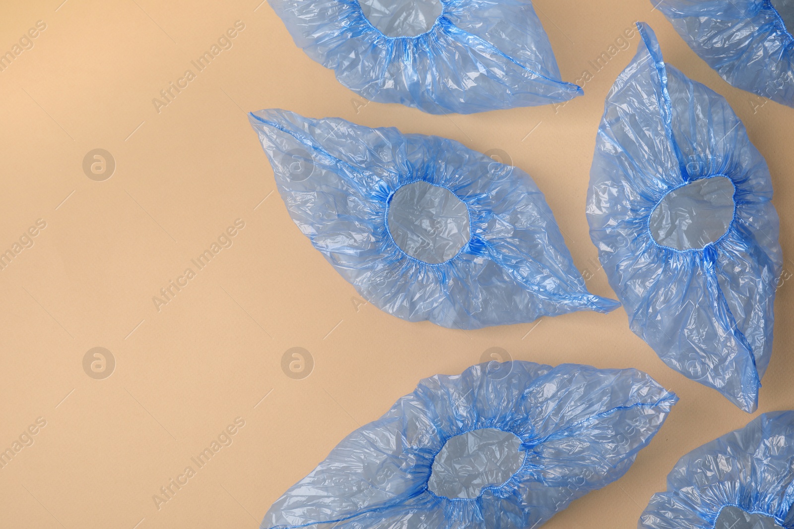 Photo of Blue medical shoe covers on beige background, flat lay. Space for text