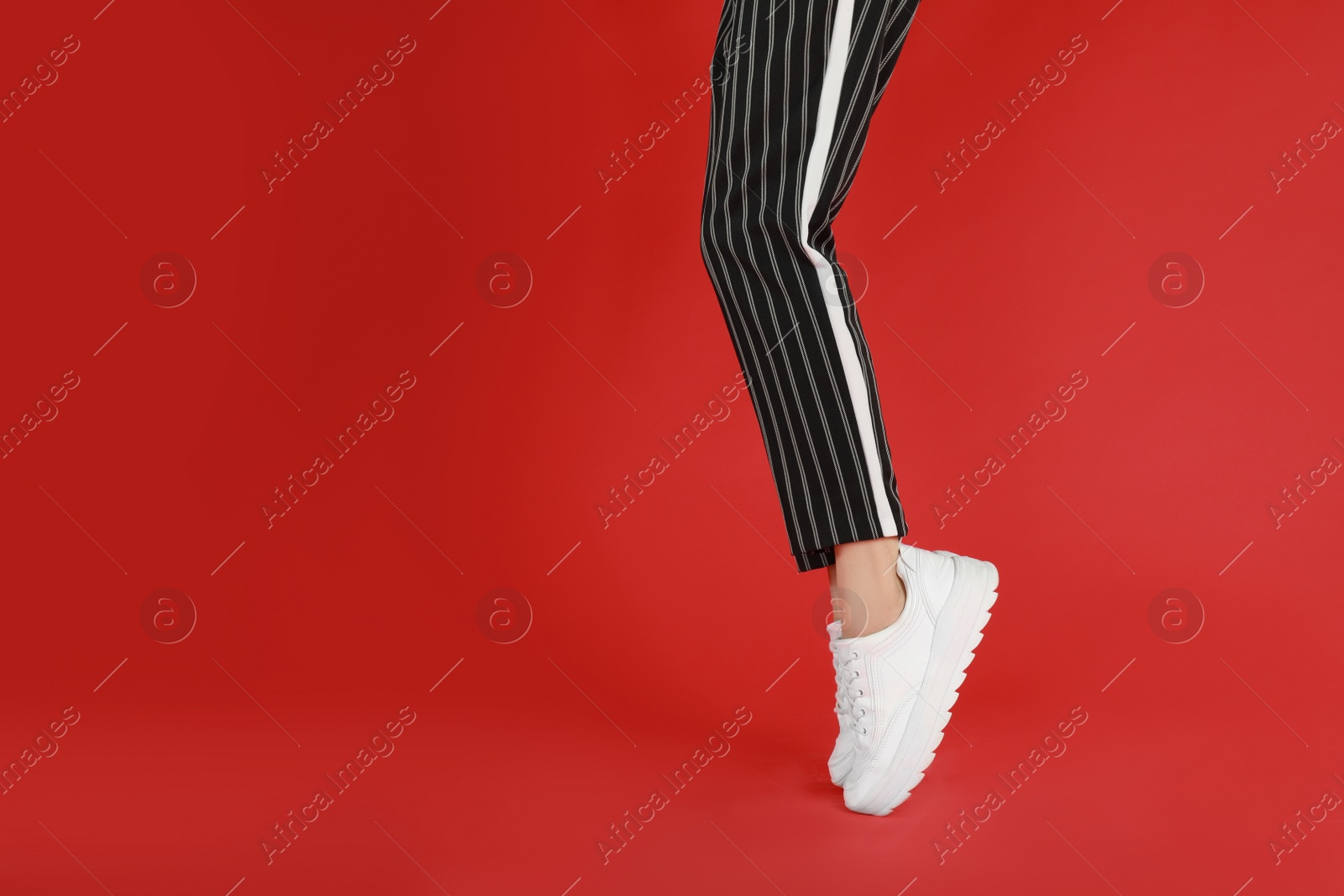 Photo of Woman in stylish sport shoes on red background. Space for text