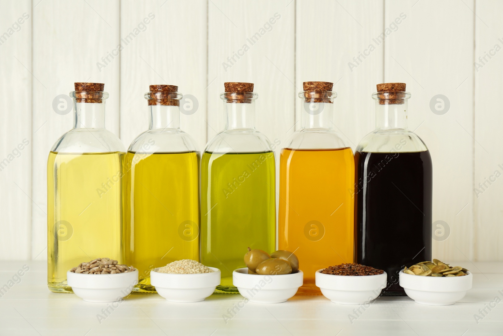 Photo of Vegetable fats. Different cooking oils in glass bottles and ingredients on white wooden table